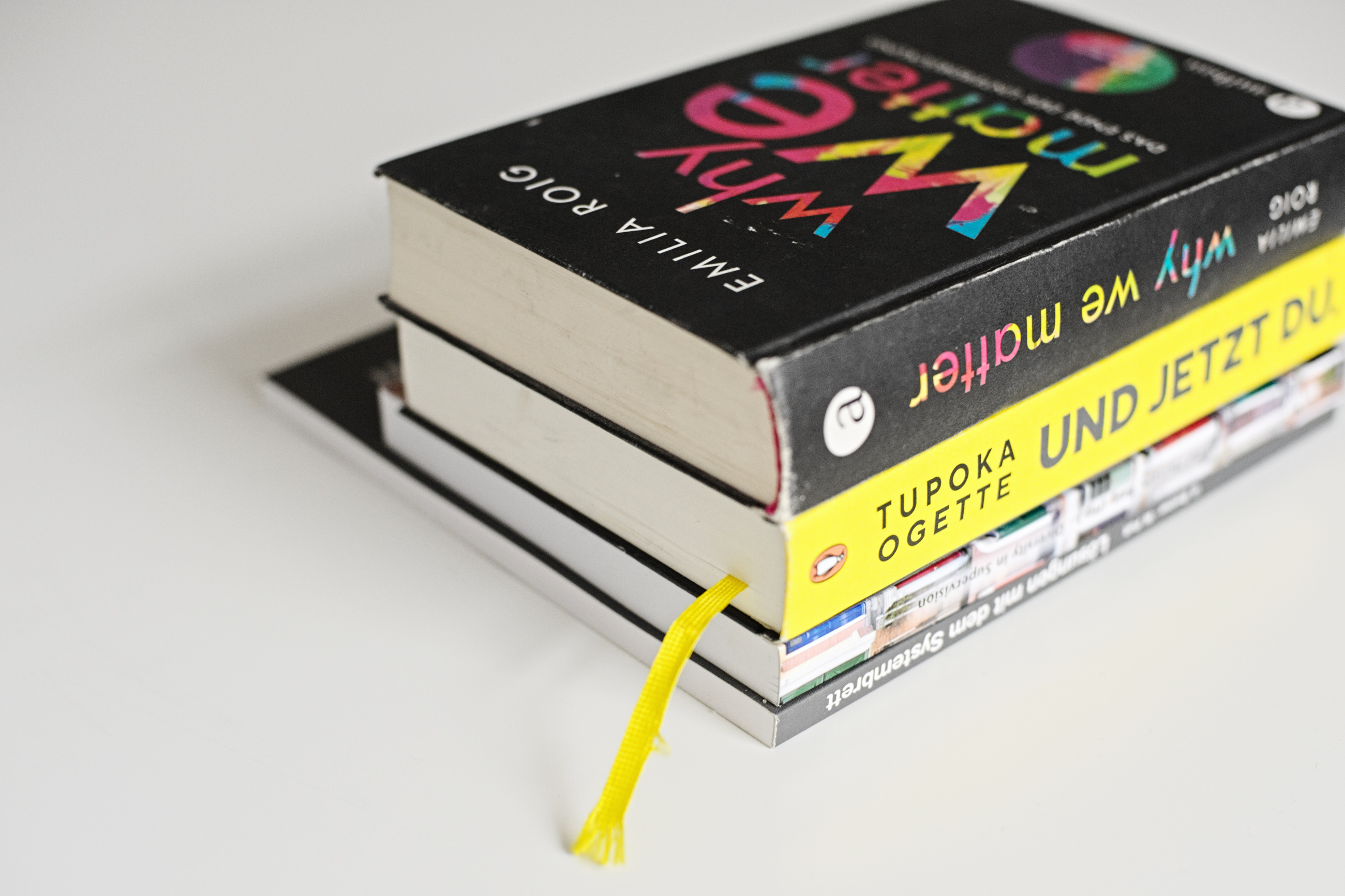Auf einem weißen Tisch liegen vier Bücher übereinander. Bei den beiden oberen Büchern ist der Text lesbar. Das obere Buch ist „Why we matter“ von Emilia Roig. Das Cover ist schwarz, der Titel in bunter Schrift  und der Name der Autorin in weißer Schrift. 